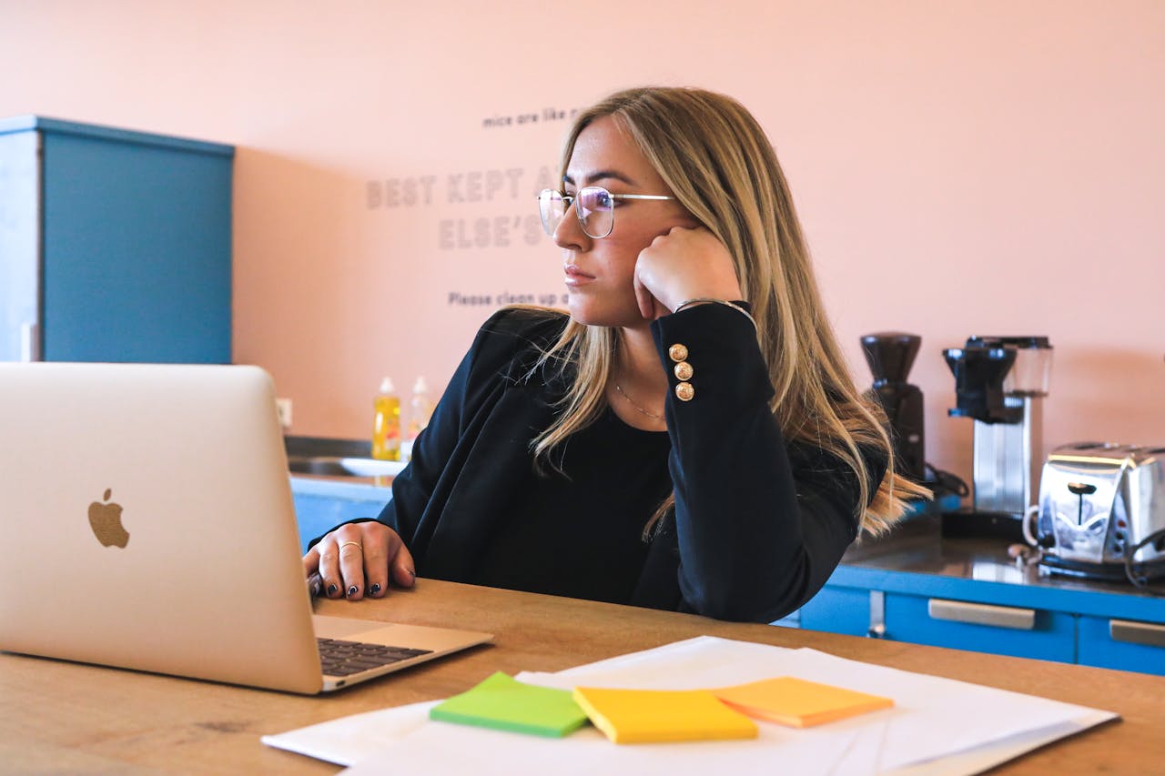 The Art of Drawing Readers In: Your attractive post title goes here Blond woman in black blazer with glasses, working on laptop in modern office.